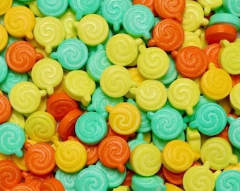 May include: A close-up shot of colorful candies in shades of yellow, orange, and teal. The candies have a spiral design with a small handle. The candies are scattered, filling the frame.