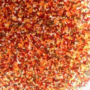 May include: A close-up of a variety of colorful sprinkles. The sprinkles are small and rectangular, and they are in shades of red, orange, yellow, and brown.