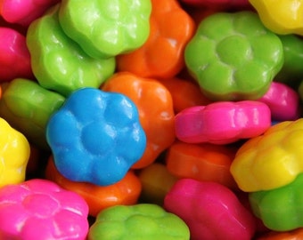 May include: A close-up of colorful candy shaped like flowers. The candy is in shades of green, blue, pink, orange, and yellow.