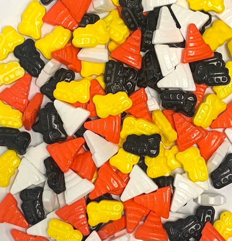 May include: A variety of colorful sprinkles in the shape of construction cones, dump trucks, and triangles. The sprinkles are perfect for decorating cakes, cupcakes, and other treats.
