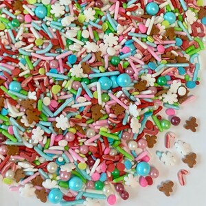 May include: A colorful mix of sprinkles for baking and decorating. The sprinkles include red, green, blue, white, pink, and brown sprinkles in various shapes and sizes. There are also small pearl-like sprinkles and candy cane sprinkles.