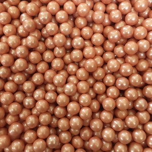 Puede incluir: Una imagen de primer plano de una gran cantidad de pequeñas pepitas redondas de color melocotón. Las pepitas tienen un brillo perlado.