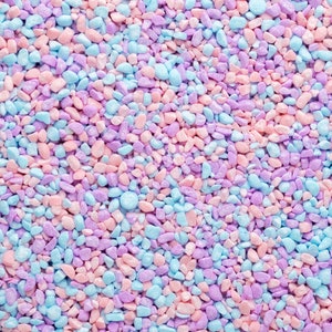 Op de afbeelding: Een close-up van een mengsel van kleine, kleurrijke kiezelsteentjes. De kiezelsteentjes zijn een mix van lichtblauw, roze en paars.