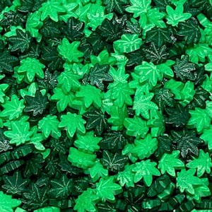 Könnte beinhalten: Nahaufnahme von grünen und dunkelgrünen Marihuana-Blattstreuseln. Die Streusel eignen sich perfekt zum Dekorieren von Kuchen, Cupcakes und anderen Desserts.