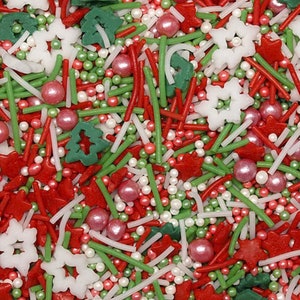 Op de afbeelding: Een feestelijke mix van kerstversieringen, met rode, groene en witte vormen. De mix bevat rode sterren en kerstbomen, groene staafjes, witte sneeuwvlokken en kleine parelachtige sprinkles in roze en wit.
