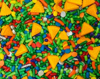 May include: A colorful mix of sprinkles, including small, long, and triangular shapes. The sprinkles are in shades of green, blue, red, orange, and yellow.