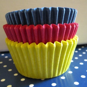 Op de afbeelding: Drie cupcake vormpjes gestapeld op elkaar. De onderste vormpje is geel, de middelste is rood en de bovenste is blauw.