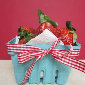 May include: A blue cardboard basket with a red and white gingham ribbon bow. The basket is filled with fresh strawberries.