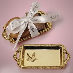 May include: Two small gold-coloured trays with decorative edges. One tray has a white ribbon tied around it with the text "Our Wedding Day" printed on the ribbon. The other tray has a dove design embossed on it.