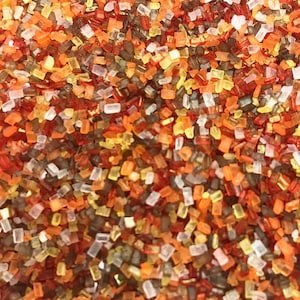 May include: A close-up of a mixture of colorful sprinkles. The sprinkles are a mix of red, orange, yellow, brown, and white. The sprinkles are small and irregular in shape.