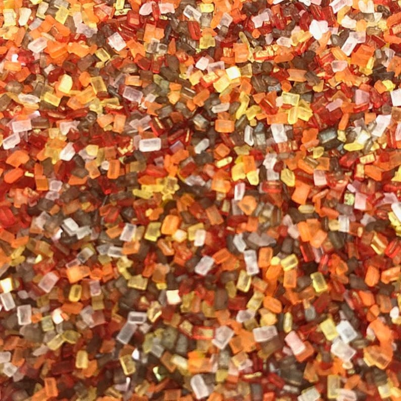 May include: A close-up of a mixture of colorful sprinkles. The sprinkles are a mix of red, orange, yellow, brown, and white. The sprinkles are small and irregular in shape.
