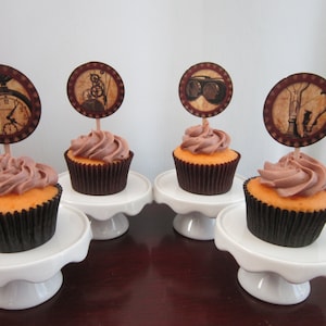May include: Four cupcakes decorated with brown frosting and topped with round paper cupcake toppers featuring vintage steampunk designs. The toppers feature images of a clock, goggles, gears, and a pipe.