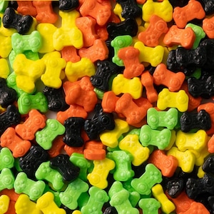 May include: A close-up of a variety of colorful candy shaped like game controllers. The candy is in shades of green, yellow, orange, and black.