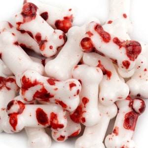 May include: A pile of white candy bones with red splatter, resembling blood, on them. The candy bones are shaped like human bones.