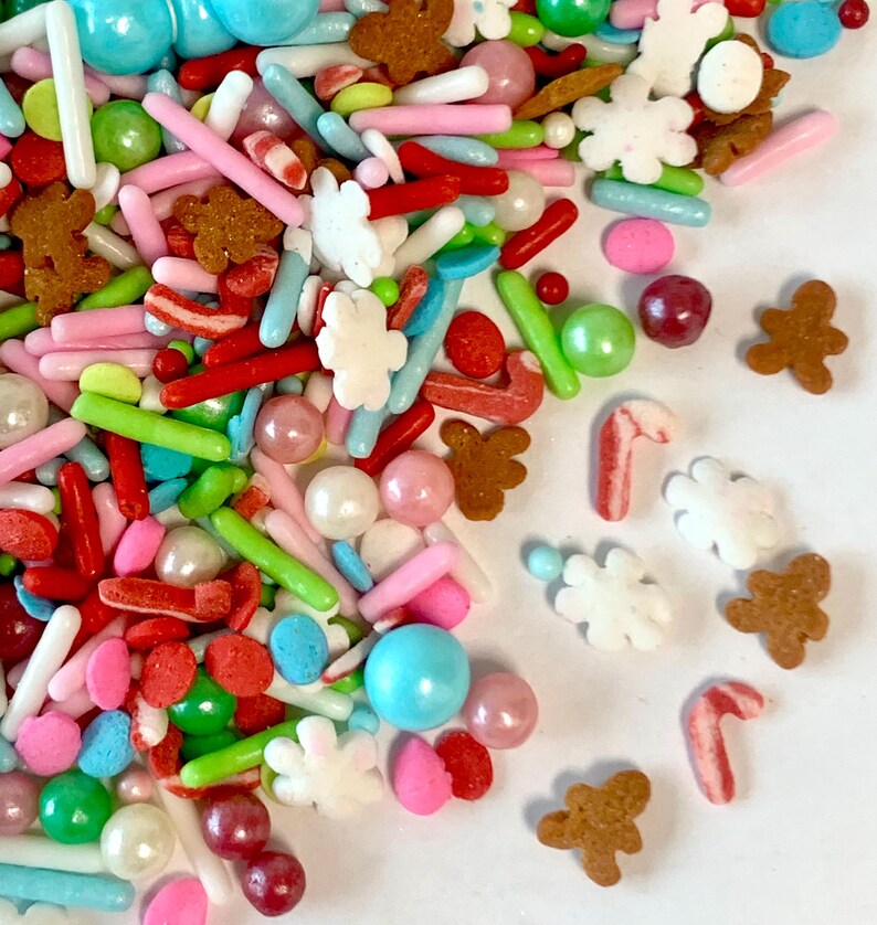 May include: A variety of colorful sprinkles, including red and white candy canes, gingerbread men, white snowflakes, and pastel-colored balls and rods.