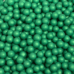 Puede incluir: Una imagen de primer plano de una gran cantidad de pequeñas bolitas de caramelo verdes redondas. Las bolitas tienen un brillo metálico.
