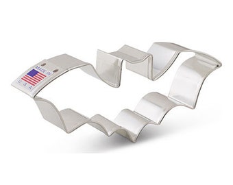 Könnte beinhalten: Ein silberner Metall-Keksstempel in Form einer Fledermaus mit einem gewellten Rand. Der Stempel hat ein "Made in USA"-Etikett an der Seite.