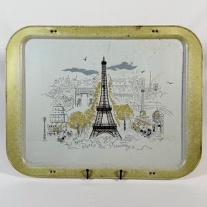 May include: A rectangular metal serving tray with a distressed gold-toned border and a white center. The tray features a black and gold illustration of the Eiffel Tower, Parisian landmarks, and the text Paris au Printemps in cursive script.