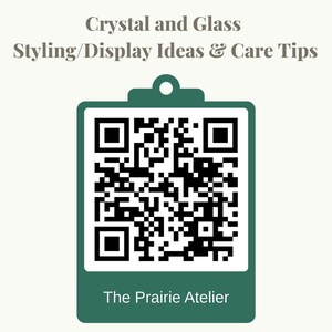 May include: A dark green clipboard graphic featuring a central black and white QR code. Above the code, the text reads Crystal and Glass Styling/Display Ideas & Care Tips. Below the code, the text reads The Prairie Atelier in white font.