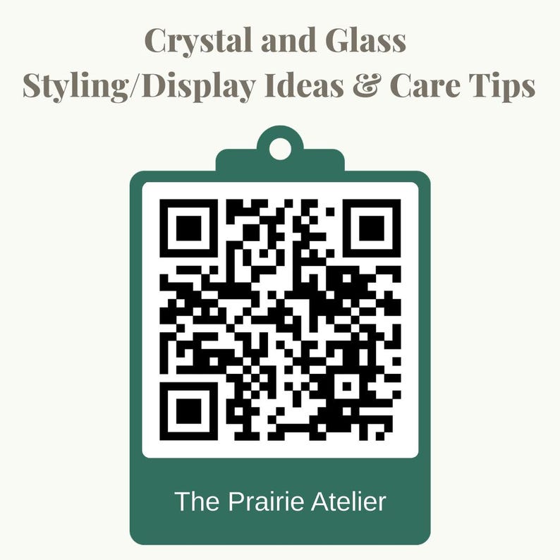 May include: A dark green clipboard graphic featuring a central black and white QR code. Above the code, the text reads Crystal and Glass Styling/Display Ideas & Care Tips. Below the code, the text reads The Prairie Atelier in white font.