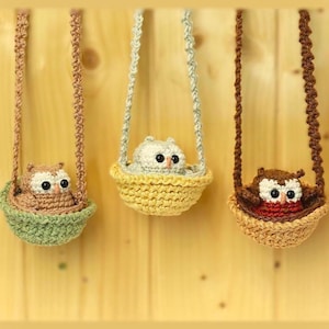May include: Three crocheted owl figurines, each nestled in a small, round, hanging basket suspended by a braided cord. The owls are brown, white, and dark brown with black eyes, while the baskets are light green, yellow, and tan.