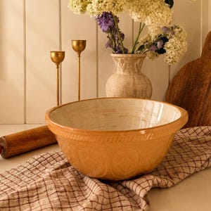 Peut inclure: Un grand bol mélangeur en céramique émaillée jaune avec un intérieur crème et des motifs en losange en relief sur l'extérieur, posé sur un tissu à carreaux beige et marron à côté d'un rouleau à pâtisserie et d'une planche à découper en bois.