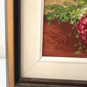 May include: Oil painting of a floral arrangement in a terracotta pot. The flowers are a deep red, with green foliage. The painting is in a white and brown wooden frame.