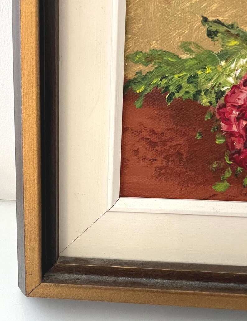 May include: Oil painting of a floral arrangement in a terracotta pot. The flowers are a deep red, with green foliage. The painting is in a white and brown wooden frame.