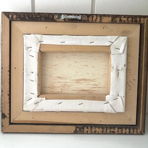 May include: Back of a framed canvas art piece. The wooden frame is a dark brown with a distressed finish. The canvas is stretched over a wooden frame and stapled in place. A metal sawtooth hanger is attached.