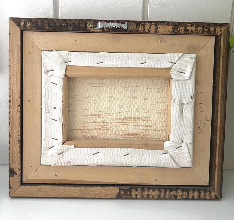 May include: Back of a framed canvas art piece. The wooden frame is a dark brown with a distressed finish. The canvas is stretched over a wooden frame and stapled in place. A metal sawtooth hanger is attached.