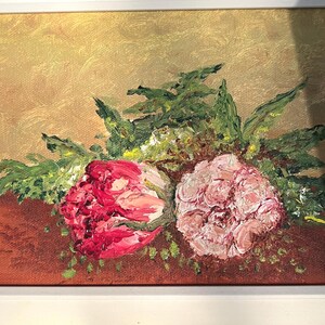 May include: Oil painting of two flowers, one red and one pink, with green foliage. The flowers are on a brown surface, set against a golden background. The artwork is framed in a white border.