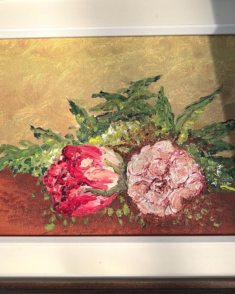 May include: Oil painting of two flowers, one red and one pink, with green foliage. The flowers are on a brown surface, set against a golden background. The artwork is framed in a white border.