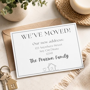 Puede incluir: Una tarjeta de anuncio blanca con el texto "WE'VE MOVED!" y los detalles de la nueva dirección. La tarjeta incluye el apellido y una ilustración de una casa. Se ve un sobre marrón y llaveros con forma de casa.