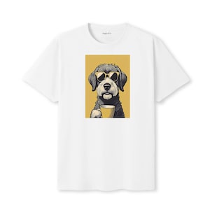 Puede incluir: Camiseta blanca con un gráfico de un perro negro con gafas de sol sosteniendo una taza amarilla. El perro está sobre un fondo amarillo. La camiseta tiene cuello redondo y mangas cortas.