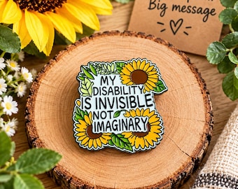 May include: A square enamel pin featuring a light blue background with the black text "MY DISABILITY IS INVISIBLE NOT IMAGINARY" surrounded by yellow sunflowers and green leaves. The pin has a dark metal border and a glossy finish.