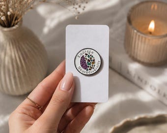 May include: A circular enamel pin featuring a white background with a split design. One side shows a purple brain illustration, while the other side displays a collection of colorful butterflies. The text Embrace Neurodiversity circles the edge.