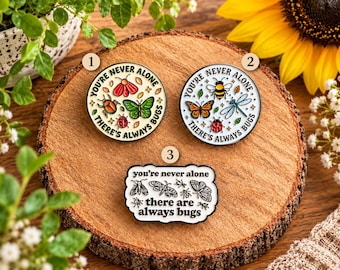 May include: Three enamel pins featuring insect illustrations and the text 'YOU'RE NEVER ALONE THERE'S ALWAYS BUGS' or 'you're never alone there are always bugs'. Two pins are circular with colorful bugs, and one is a rectangular shape with black line art.