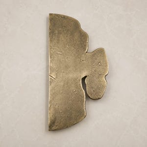 Peut inclure: Un objet en laiton massif présentant un bord vertical plat et droit d'un côté et un contour irrégulier, organique et ondulé de l'autre. La surface possède une finition métallique texturée et patinée avec des tons dorés et bruns.