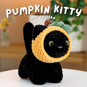 Könnte beinhalten: Ein gehäkeltes schwarzes Katzen-Plüschtier mit einer gelben, kürbisförmigen Kapuze mit grünem Stiel und Blatt. Der Text PUMPKIN KITTY PDF PATTERN steht in weißen Buchstaben über der Katze. Die Katze hat leuchtend grüne Augen und eine kleine weiße Nase.