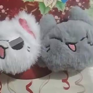 May include: Two plush animal face pillows. One is white with pink ears and sunglasses, the other is gray. Both have embroidered faces with open mouths and tongues sticking out.