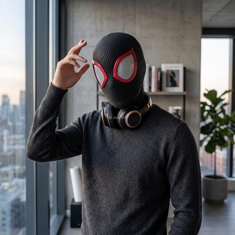 May include: Black Spider-Man mask with red trim around the eye openings. The mask has a textured pattern and covers the entire head and neck. The person is wearing a dark gray sweater and headphones.