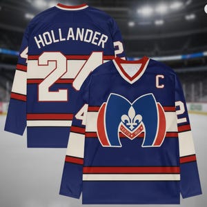 May include: A blue hockey jersey with white and red accents. The jersey features the name "HOLLANDER" and the number "24" on the back. The front displays a logo with a fleur-de-lis and the text "ESTD 1903". The jersey has a "C" on the chest.