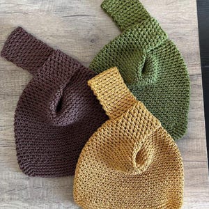 May include: Three handmade knitted bags in shades of brown, olive green, and mustard yellow. Each bag features a unique handle design and a textured, open-weave pattern, perfect for carrying essentials.