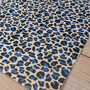 Könnte beinhalten: Ein rechteckiges Blatt Papier mit Leopardenmuster. Das Muster zeigt schwarze und blaue Flecken auf cremefarbenem Hintergrund. Das Papier liegt auf einer hellbraunen Holzoberfläche.