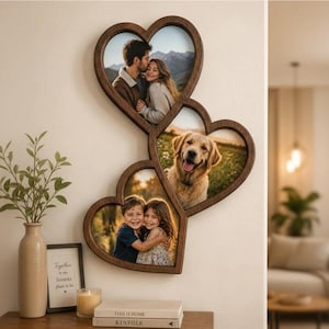 Op de afbeelding: Een aan de muur gemonteerde fotolijst van donker hout bestaande uit drie met elkaar verbonden hartvormige openingen. Het bovenste hart toont een koppel, het middelste hart een golden retriever en het onderste hart twee kinderen die elkaar omhelzen.