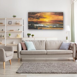 Könnte beinhalten: Ein Wohnzimmer mit einem Gemälde eines Sonnenuntergangs über dem Meer. Das Kunstwerk mit warmen Orange- und Gelbtönen hängt über einem beigen Sofa. Ein Sessel und ein Teppich sind ebenfalls zu sehen und schaffen einen komfortablen Wohnraum.