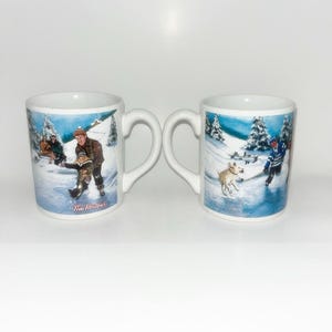 May include: Two white ceramic mugs featuring winter scenes. The left mug shows people skating with the text Tim Hortons. The right mug depicts a person playing hockey with a dog on ice. Both mugs have a handle and a snowy landscape illustration.