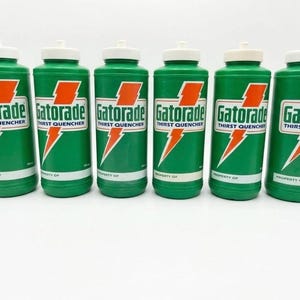 May include: Six green plastic Gatorade Thirst Quencher squeeze bottles with white screw-top lids. Each bottle features the orange lightning bolt logo, the Gatorade Thirst Quencher text, and a white label area at the bottom labelled Property Of.