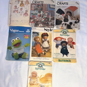 Peut inclure: Un ensemble de sept pochettes de patrons de couture présentant divers modèles, dont Simplicity 727, McCall's Crafts 2690 et 2504, Vogue Patterns 598 Muppet Babies, Style 2011, et les patrons Butterick Cabbage Patch Kids 330 et 337.