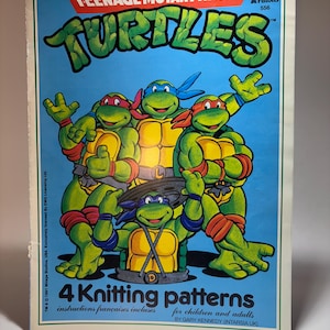 May include: A Teenage Mutant Ninja Turtles knitting pattern booklet with a blue cover featuring four green turtles with colored masks. The text reads Teenage Mutant Ninja Turtles, 4 Knitting patterns, instructions françaises incluses, and for children and adults.